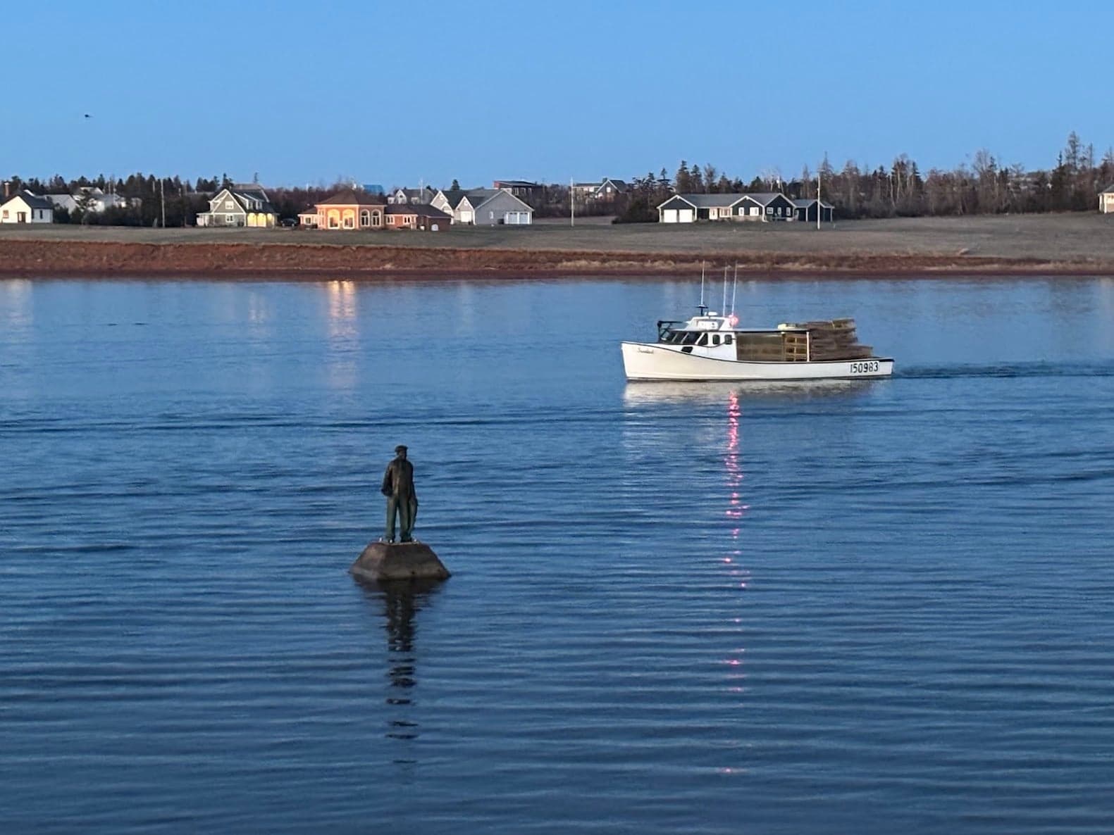 A fishing boat passing a statue in North Rustico Harbour